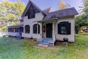 A two-story house with a porch, a front door, and a barbecue grill in the yard.