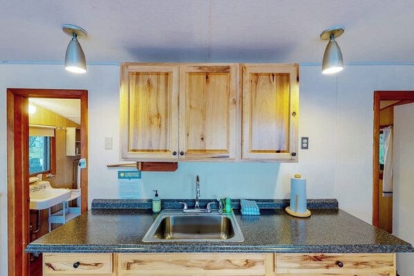 Une cuisine dotée de meubles en bois, d’un plan de travail en granit, d’un évier en acier inoxydable et de deux luminaires suspendus.