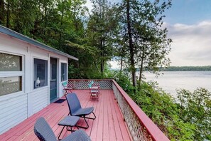 Une terrasse couverte, dotée de chaises et d’une table, qui offre une vue sur une étendue d’eau et est entourée d’arbres.