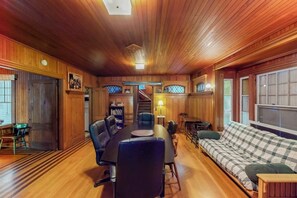 Una habitación con paneles de madera, una mesa de comedor, sillas, un sofá y una escalera.