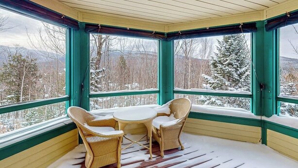 A covered porch with wicker furniture and large windows. - Spacious Mountain Retreat at Smugglers' Notch Resort w/ Great Views, Pool Access (Jeffersonville)