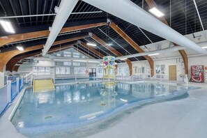 Ein überdachter Pool mit hoher Decke, sichtbaren Trägern und einem Rettungsschwimmerstand.