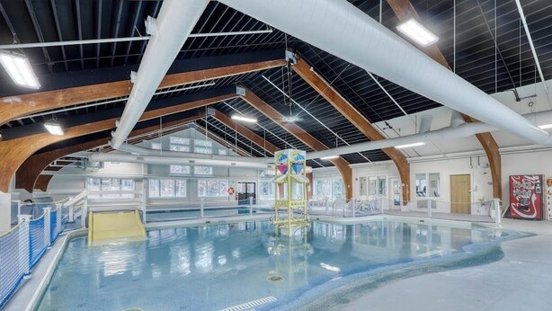 Ein Innenpool mit hoher Decke, Holzbalken und freiem Blick auf den Poolbereich.