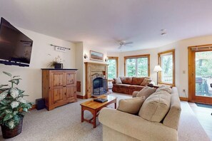 A living room with a fireplace, a sofa, a television, and a ceiling fan.