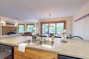 A kitchen with a large island, double sink, and a dining area with chairs and a chandelier.