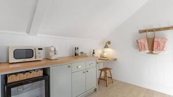 Een keuken met een magnetron, koffiezetapparaat en een klein krukje.