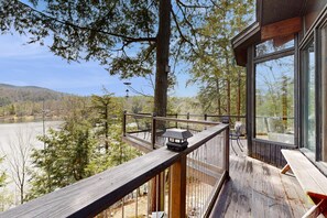 Eine Holzterrasse mit Geländer, mit Blick auf einen See und bewaldete Hügel.