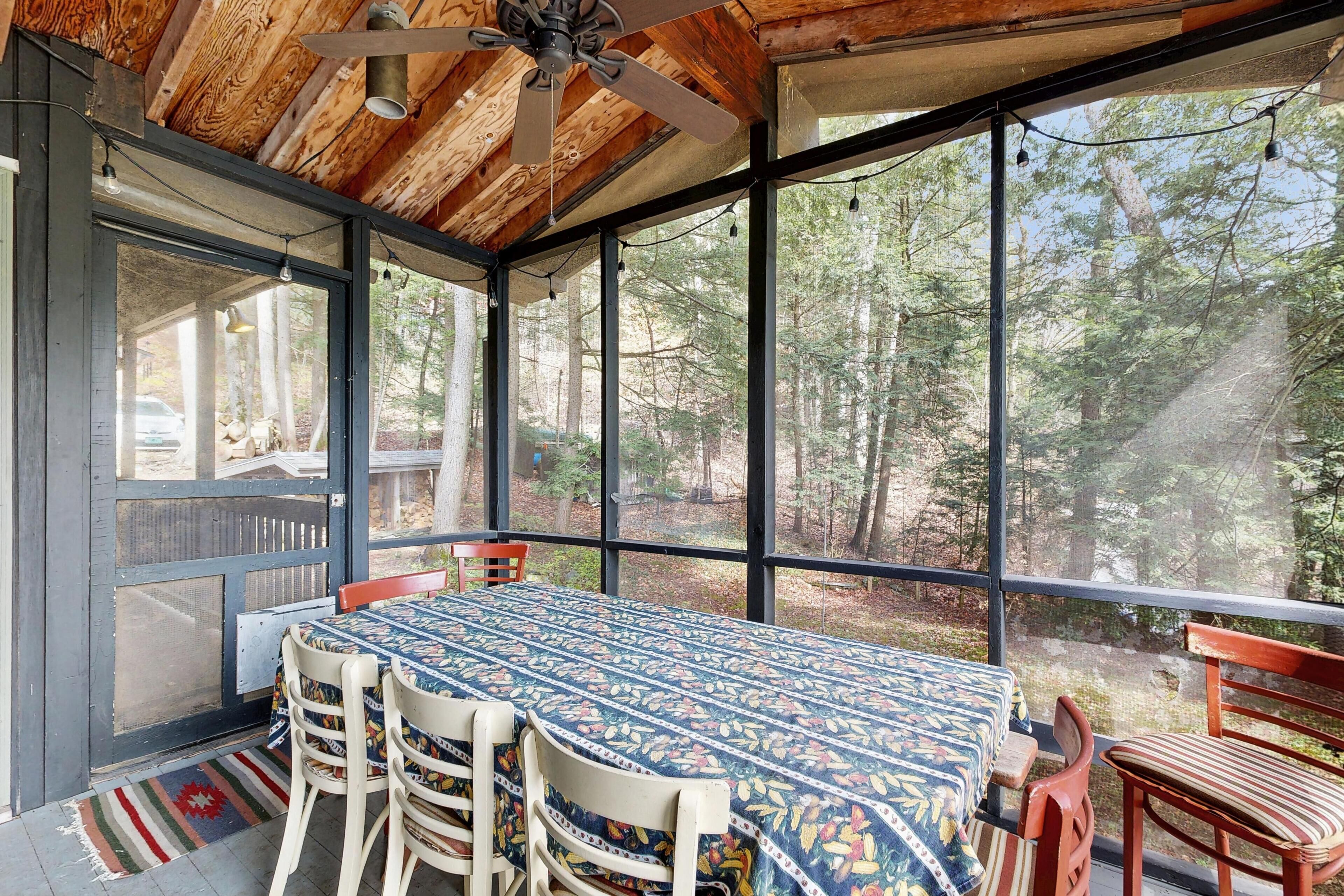 A covered outdoor dining area with a table and chairs, large windows, and a ceiling fan.