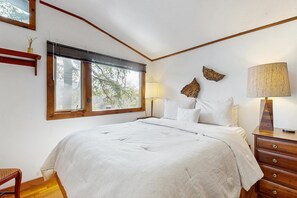 Ein Schlafzimmer mit einem großen Bett, einem Nachttisch, einer Lampe und einem Fenster mit Jalousien.