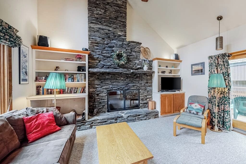 Una sala de estar con chimenea de piedra, un sofá, una mesa de centro, un televisor y una estantería.