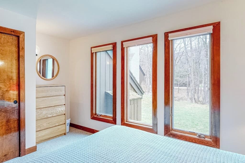 A bedroom with a bed, a dresser, a mirror, and three windows.
