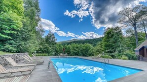 Una piscina con sillones de descanso, rodeada de árboles y un cielo despejado.