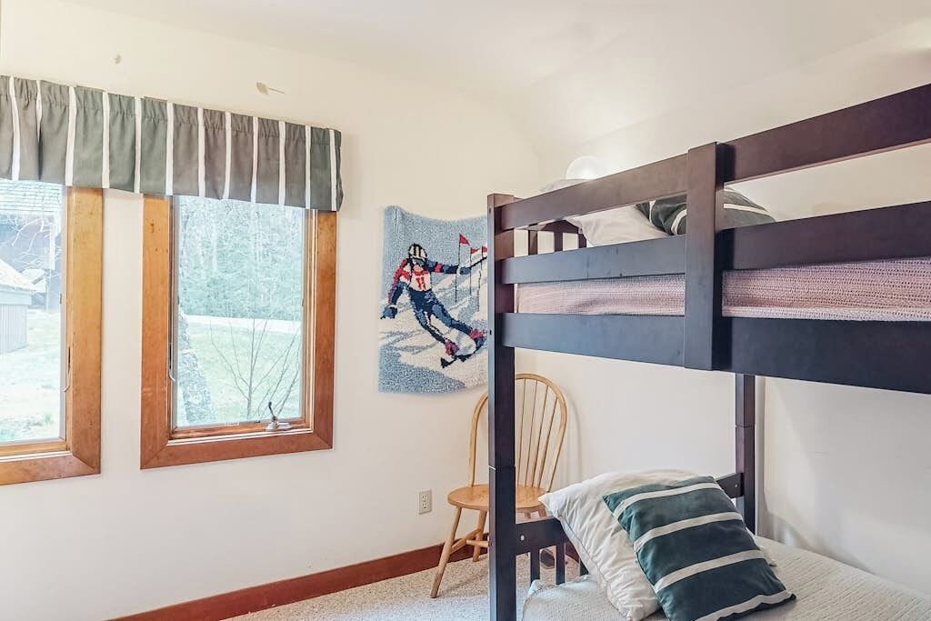A bunk bed room with a window, a chair, and a wall art piece.
