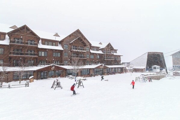 A large wooden lodge with multiple stories and a ski slope in front.