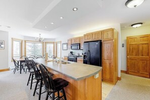 A modern kitchen with wooden cabinets, a large island with bar stools, a black refrigerator, and a microwave.
