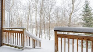 A wooden deck with snow-covered railings and a view of a snowy forest.