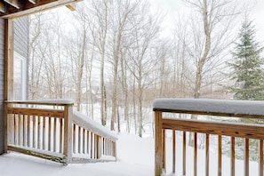 Eine Holzterrasse mit schneebedeckten Geländern und Blick auf einen verschneiten Wald.
