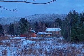 A cabin with a snow-covered roof, surrounded by trees and a hill in the background. - Mountain view house w/ two fireplaces, BBQ, w/d, jacuzzi, wifi, a/c (Elmore)