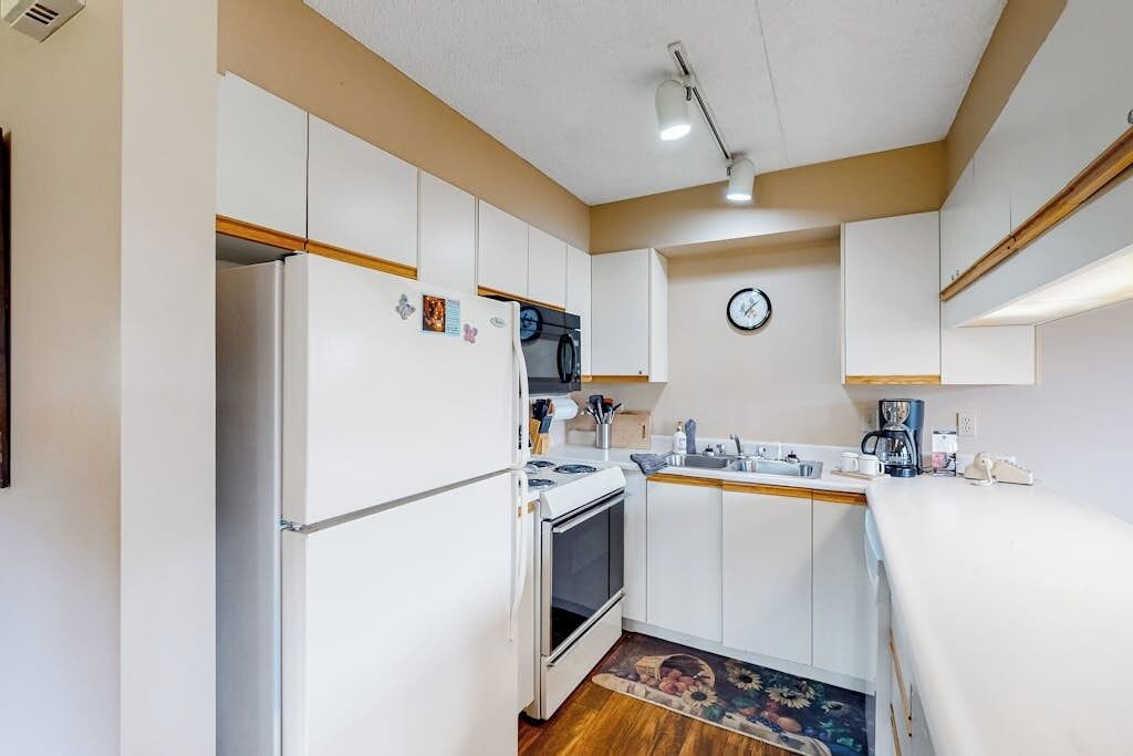 A compact kitchen with white cabinets, a refrigerator, stove, and a clock on the wall.