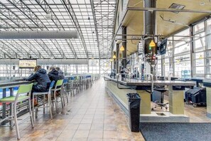 Ein heller Wartebereich mit Tischen, Stühlen und einer Theke, ausgestattet mit einem großen Fenster.