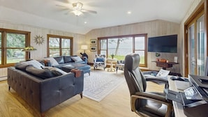 A spacious living room with a large sofa, a chair, a TV, and a desk.