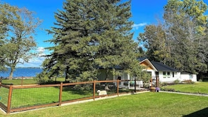 A house with a fenced yard, a large tree, and a view of the water.