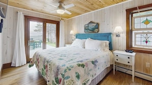 A bedroom with a bed, a ceiling fan, a nightstand, a window with a stained glass design, and a view through a glass door.