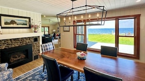 A dining area with a wooden table and chairs, a fireplace, and a view of the ocean.