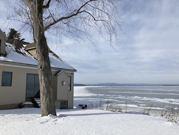 A house with a snow-covered yard and a view of a frozen body of water. - Lakeside retreat with grill, fireplace, W/D, AC & sunset views - dog-friendly (Colchester)