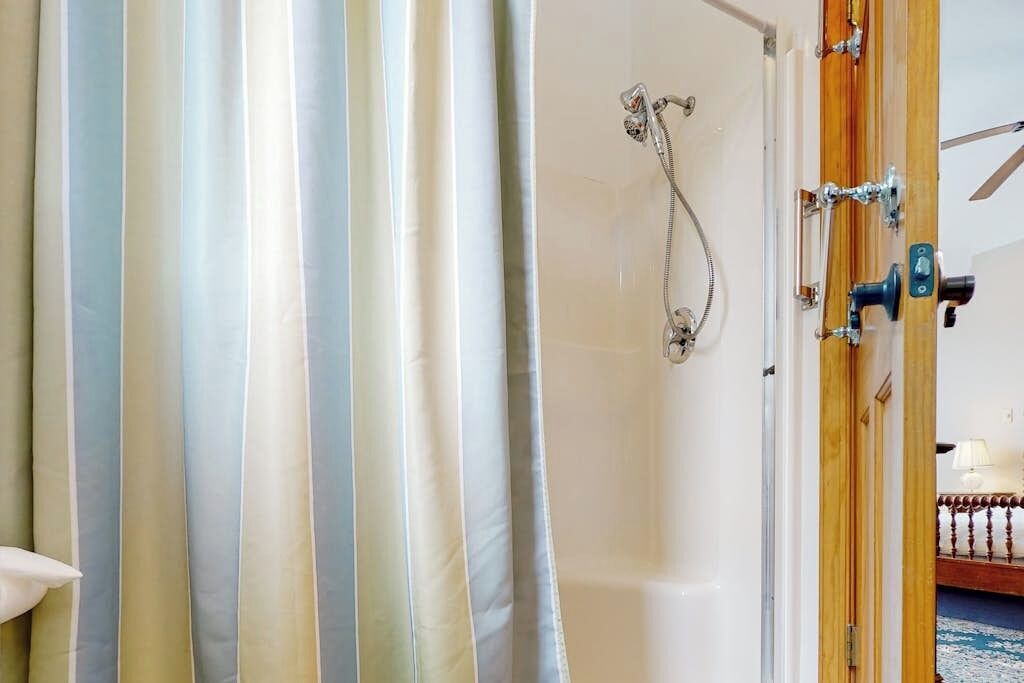A bathroom with a bathtub, shower, striped curtains, and a wooden door.