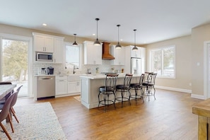 A spacious kitchen with white cabinetry, a central island with bar stools, pendant lighting, and large windows. - Lakeside retreat with grill, fireplace, W/D, AC & sunset views - dog-friendly (Colchester)