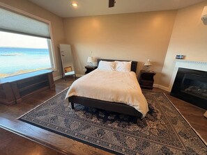 A bedroom with a large bed, a fireplace, a nightstand, a mirror, and a view of the ocean. - Lakeside retreat with grill, fireplace, W/D, AC & sunset views - dog-friendly (Colchester)