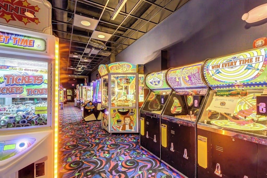 A row of arcade machines with ticket redemption options, a patterned floor, and a ceiling with visible beams.
