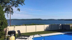 En swimmingpool med udsigt til en sø, grill og en stol.