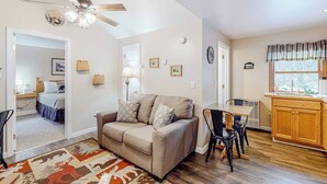 Un salon avec un canapé, une table à manger avec des chaises, un ventilateur de plafond et un coin cuisine doté de meubles en bois et d’une fenêtre.