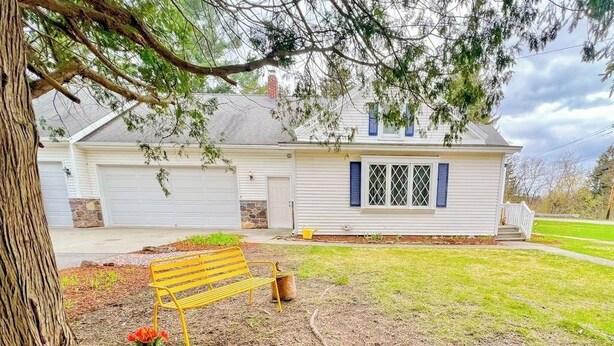 Une maison à deux étages avec un garage, un porche à l’avant et une cour comprenant un banc et un pot de fleurs.