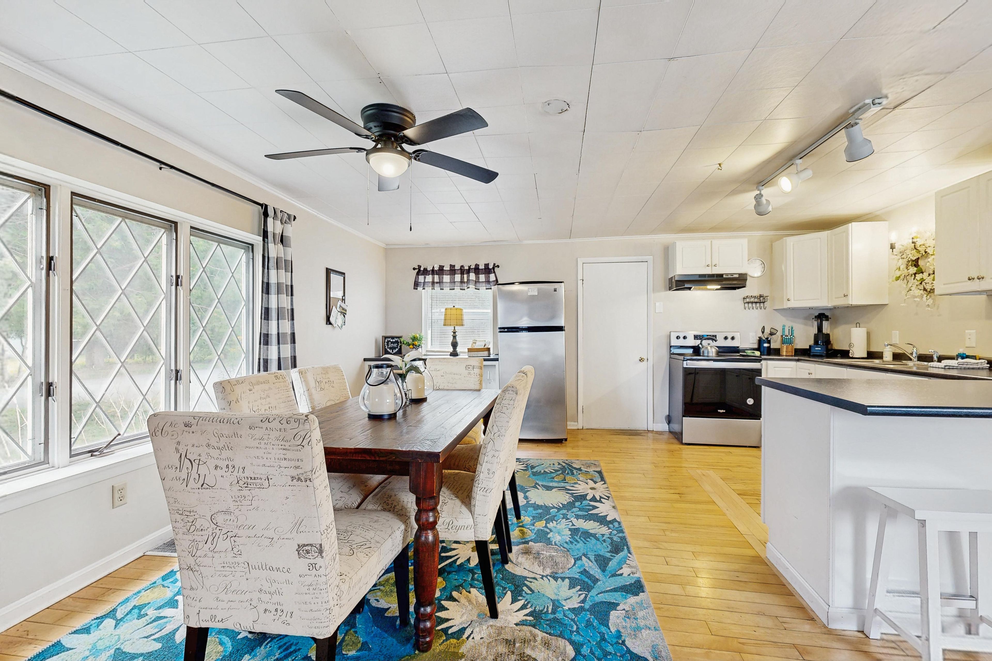 A kitchen with a dining area, wooden flooring, a ceiling fan, and a window with a view.