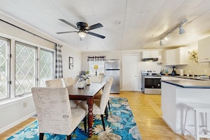 A kitchen with a dining area, wooden flooring, a ceiling fan, and a window with a view.
