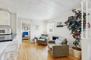 A modern living room with a sofa, armchairs, a dining area with a microwave, and a large potted plant.