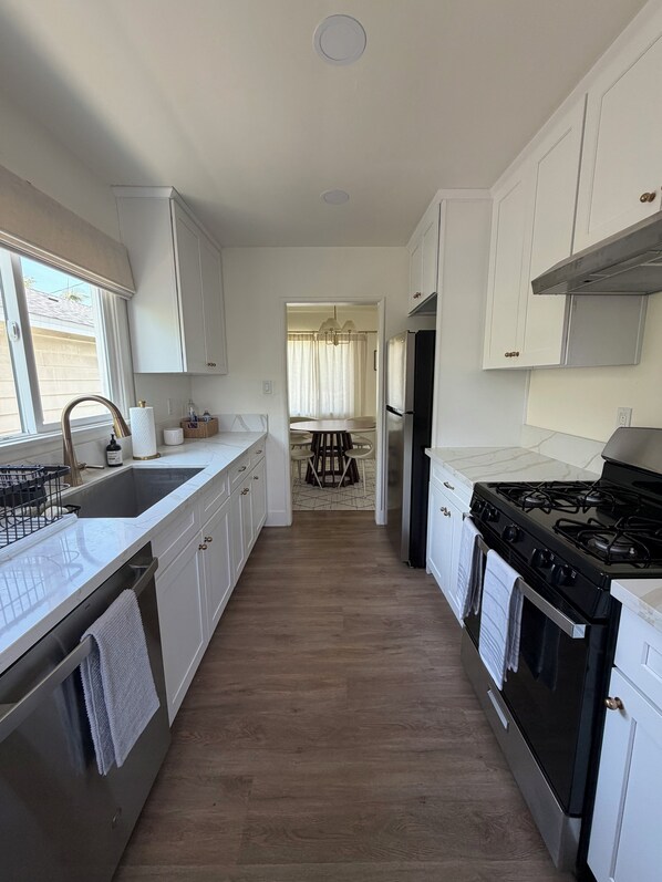 Una cocina con gabinetes blancos, un lavamanos de acero inoxidable, una estufa a gas y un refrigerador.