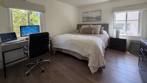 Une chambre à coucher avec un lit, un bureau avec un ordinateur, une chaise et une fenêtre donnant sur un paysage verdoyant.