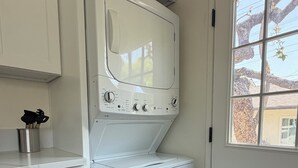 Une buanderie équipée d’un lave-linge et d’un sèche-linge à chargement frontal, d’un meuble avec un tiroir et d’une fenêtre donnant sur les arbres.