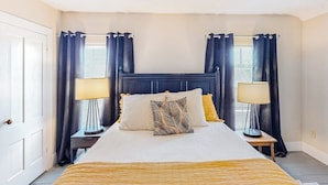 Une chambre à coucher bien rangée, avec un lit, deux tables de chevet et une fenêtre avec des rideaux.