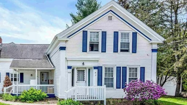 Une maison à deux étages avec un porche à l’avant, un petit jardin et une boîte aux lettres.