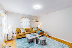 Un salon comprenant un canapé, une table basse et un pouf, une lampe et une fenêtre avec des rideaux.