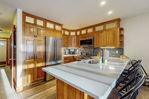 Eine moderne Küche mit Holzschränken, einem Edelstahlkühlschrank, einer Mikrowelle und einer großen Kochinsel mit Barhocker.