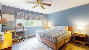 A bedroom with a bed, desk, chair, and a ceiling fan.