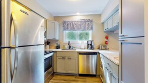 A compact kitchen with stainless steel appliances, a dishwasher, and a window with a patterned valance.