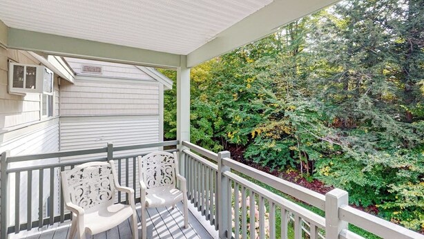 A covered porch with two white chairs, a white railing, and a view of dense green foliage.