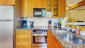 Cocina con armarios de madera, refrigerador de acero inoxidable, microondas, horno, encimeras de granito y un lavamanos.